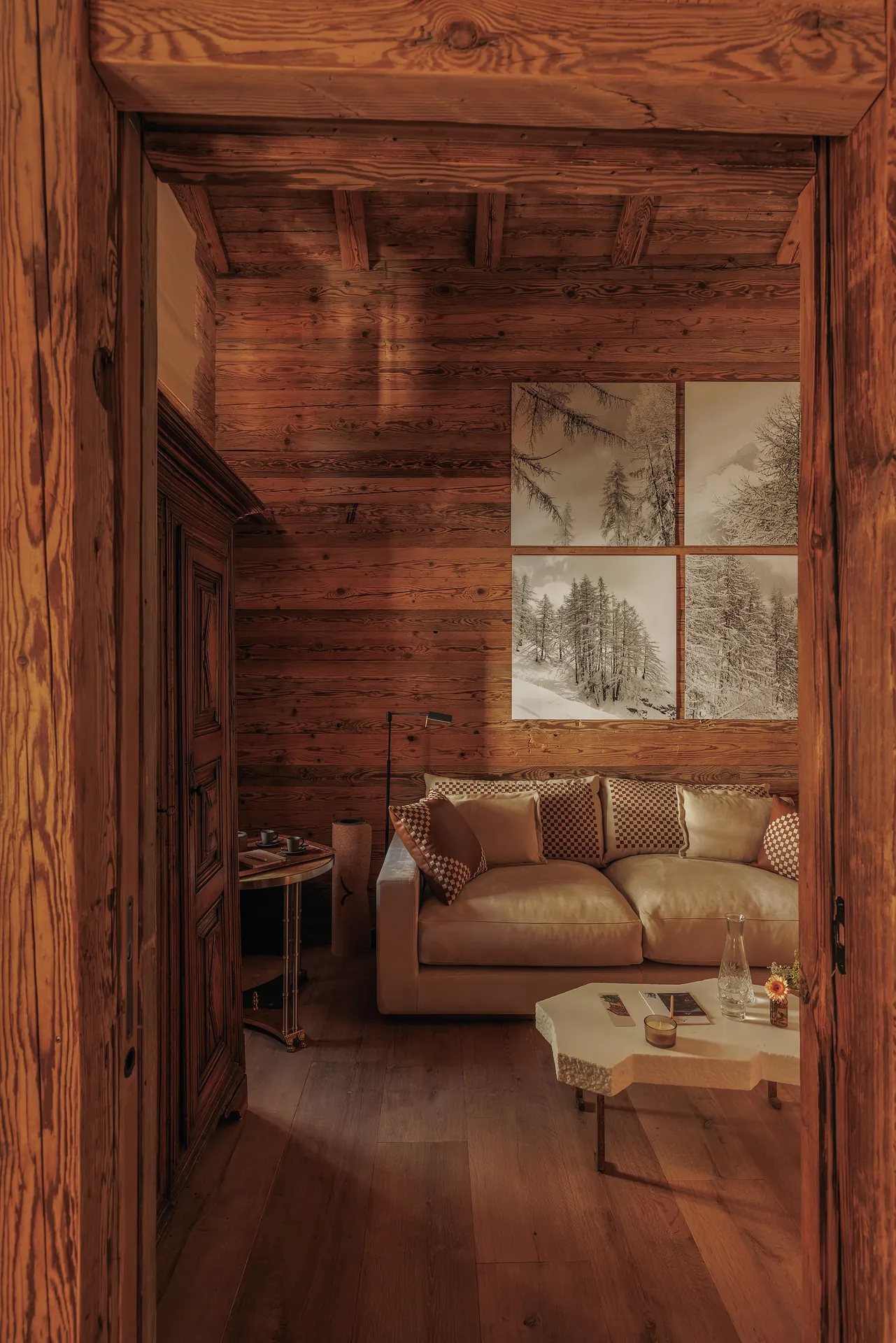 Living room with a cream sofa, checkered cushions and a four-panel winter forest photograph on a log wall