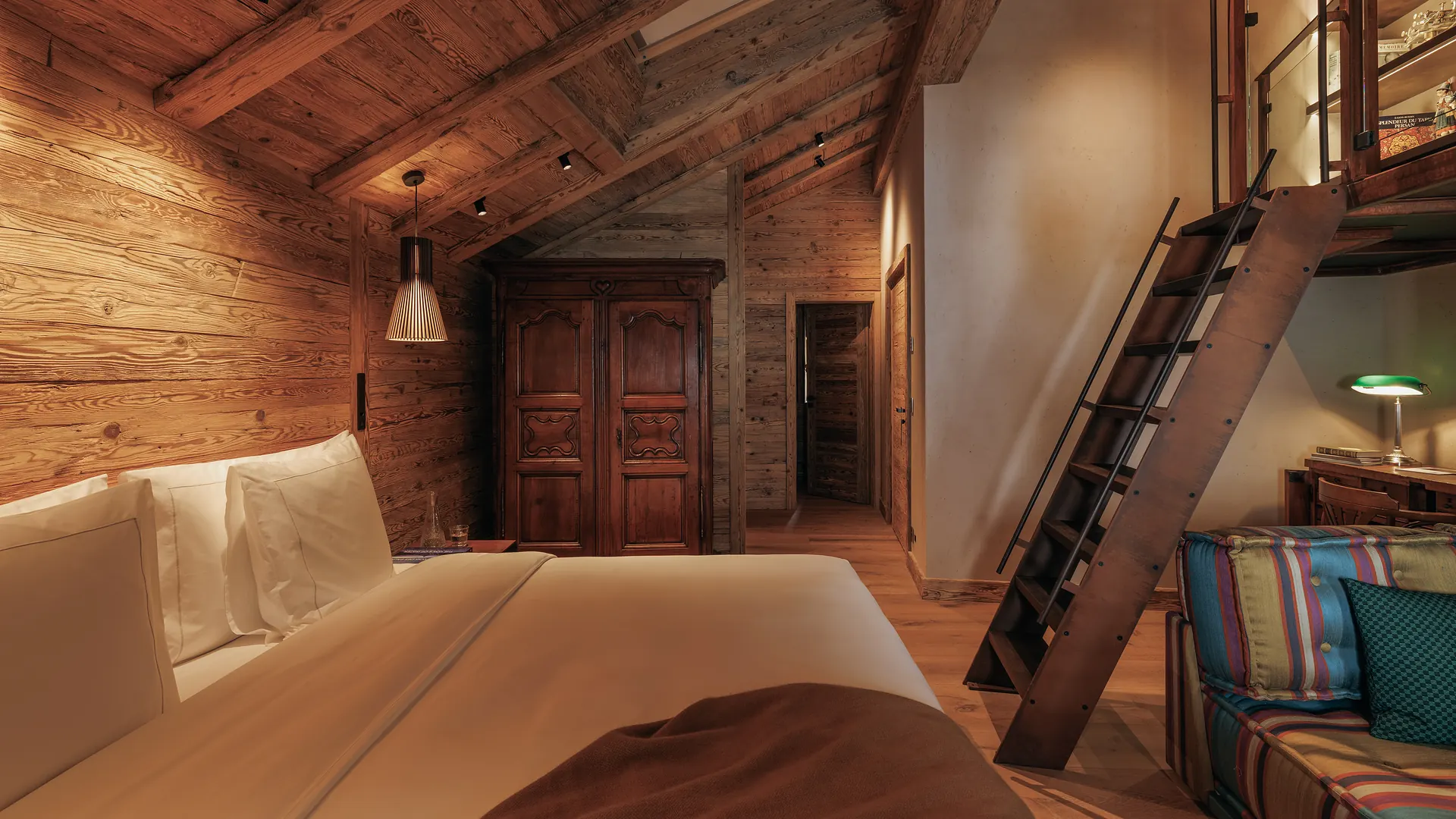Full room overview showing the bed, carved armoire, mezzanine ladder, striped sofa and library shelves above