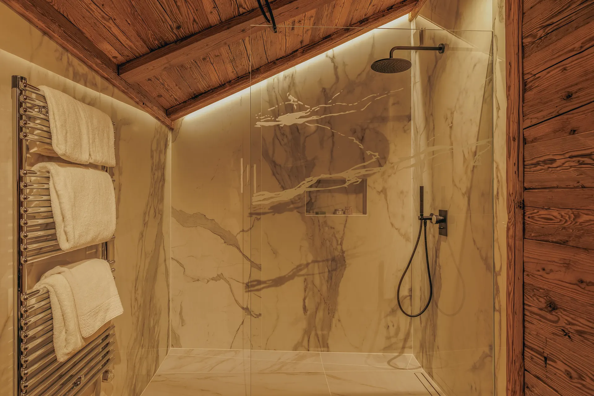 Begehbare Dusche mit dramatisch geäderten Marmorwänden, einer mattschwarzen Regendusche und bernsteinfarbener indirekter Beleuchtung unter einer Decke aus Baumstämmen