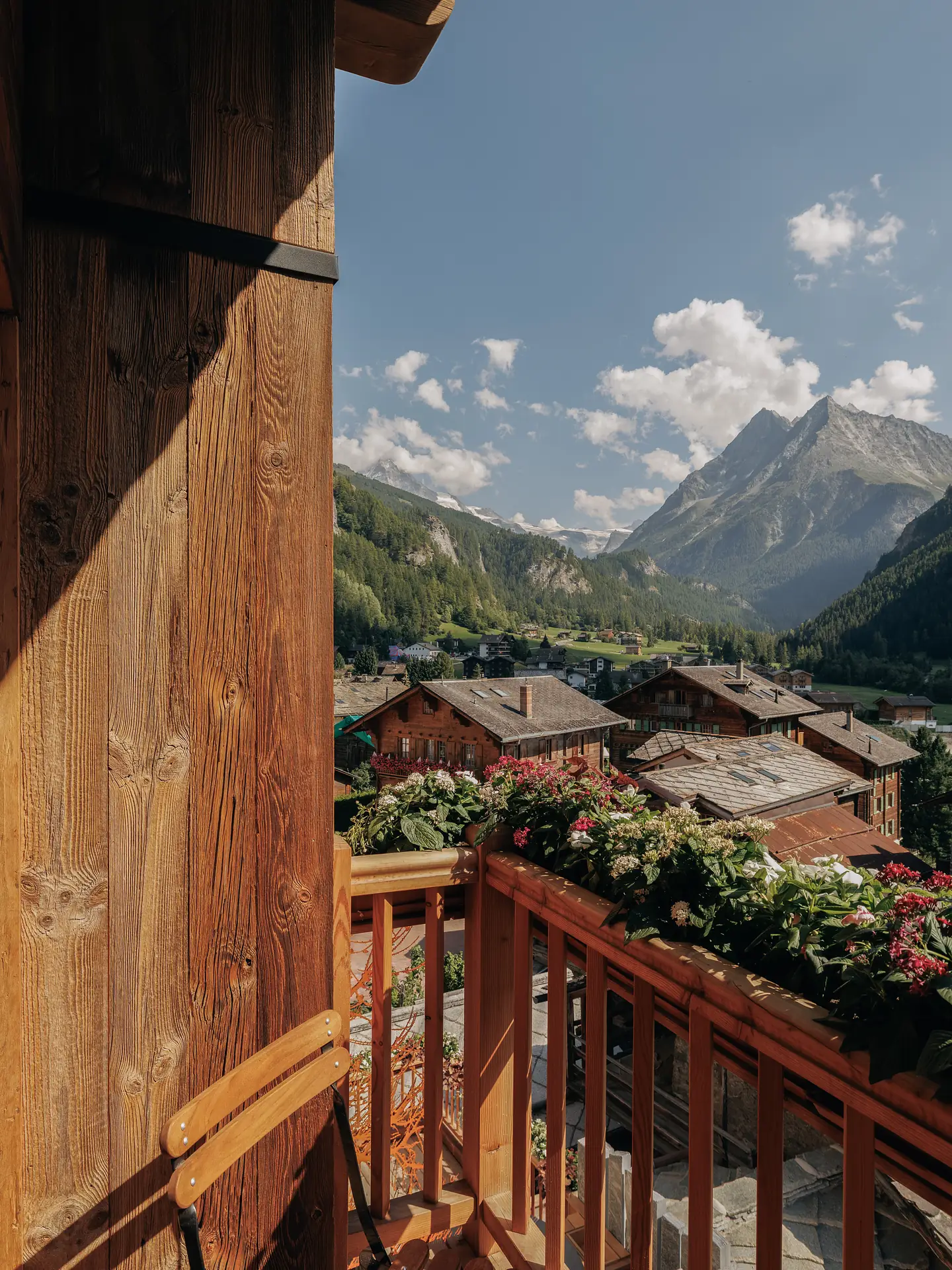 Balcony view over the rooftops of an alpine village with flower boxes and snow-capped peaks in the background