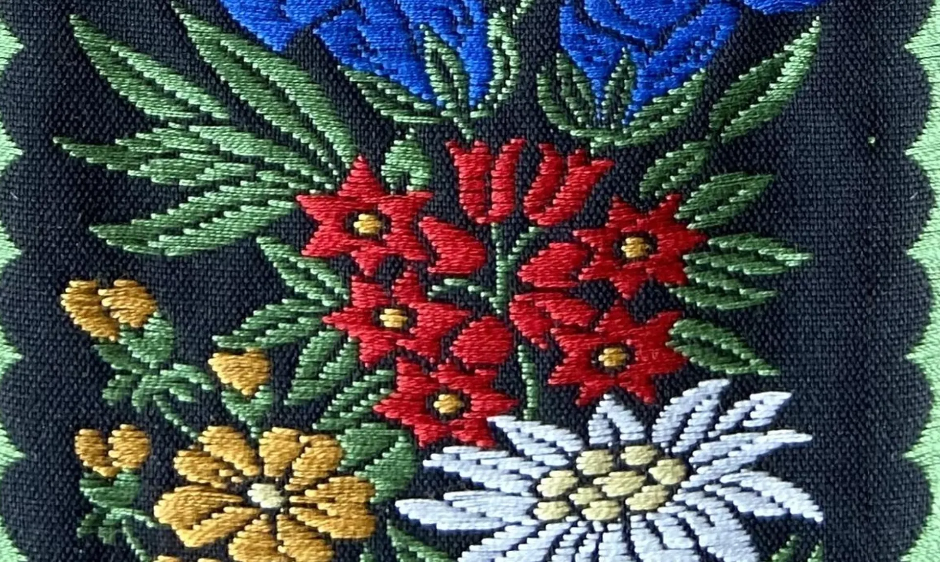 Close-up of an embroidered textile with alpine flowers including red edelweiss and blue gentian on a dark background