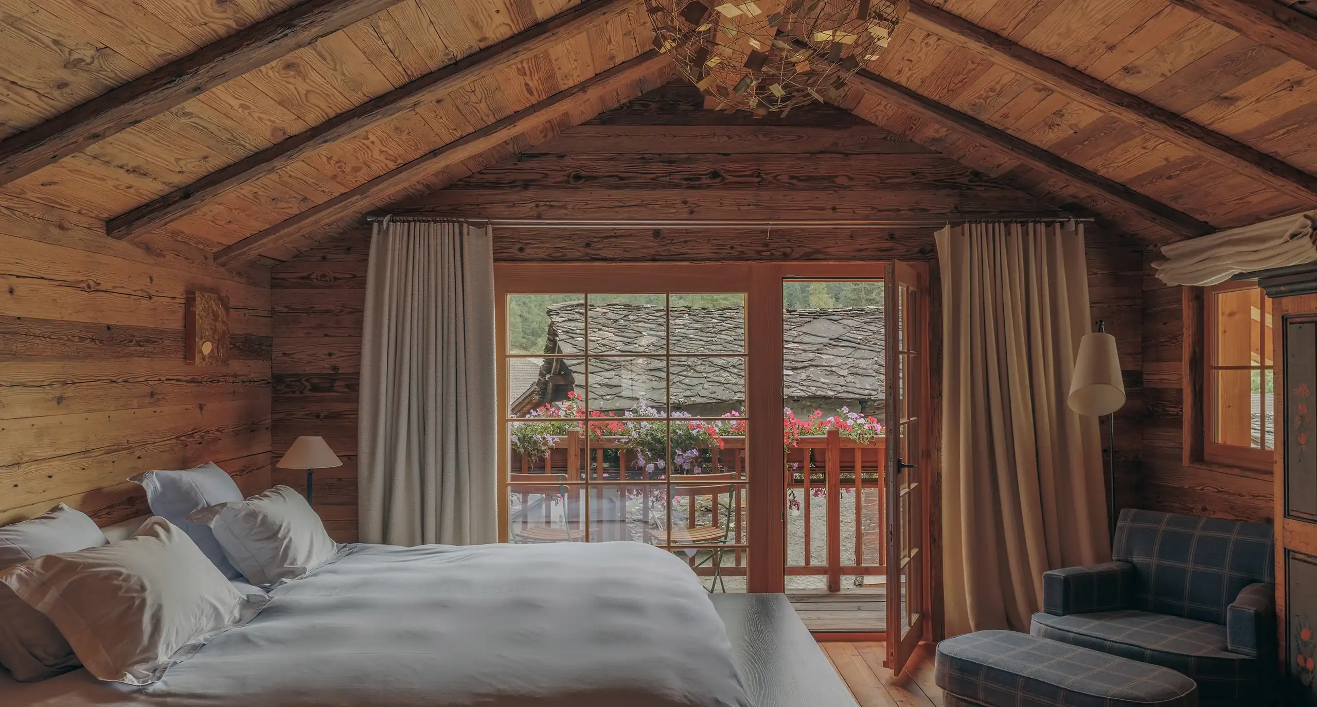 Wood-beamed attic bedroom with a bed facing open doors to a flower-lined balcony