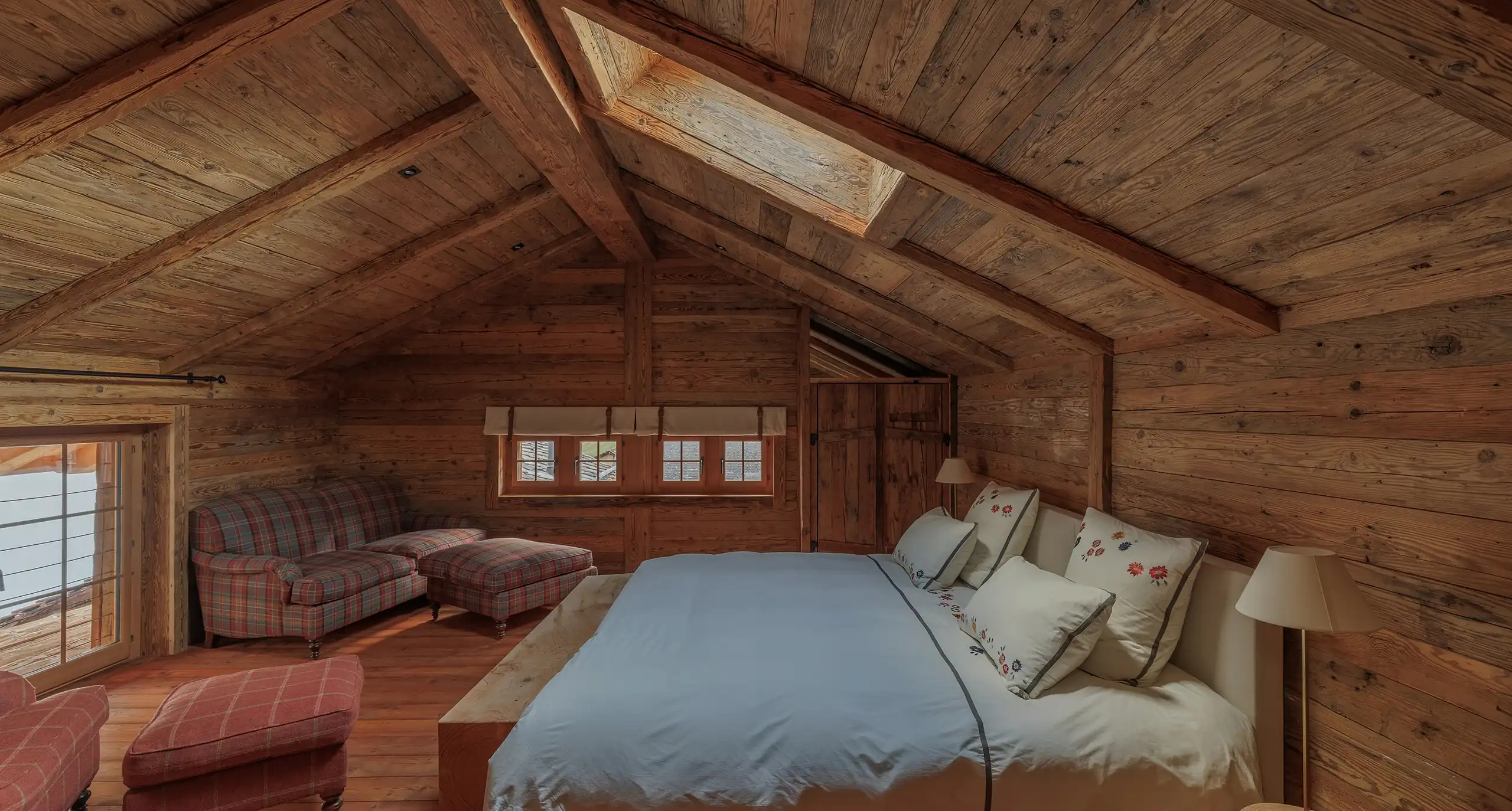 Vaulted wooden attic bedroom with a skylight and plaid armchairs