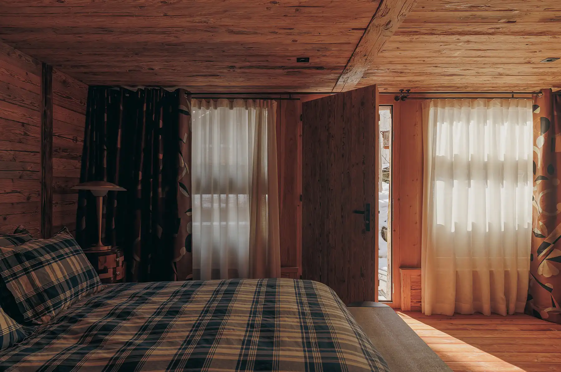 Wood-paneled bedroom with a plaid bedspread and a door open to snowy outdoors