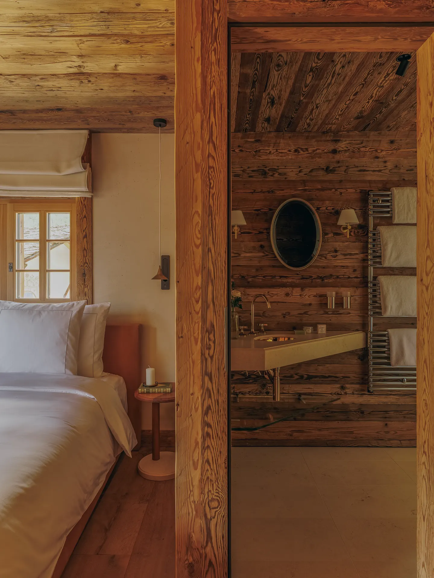 Bed with white linens beside an open doorway to a wood-paneled bathroom with a stone washbasin