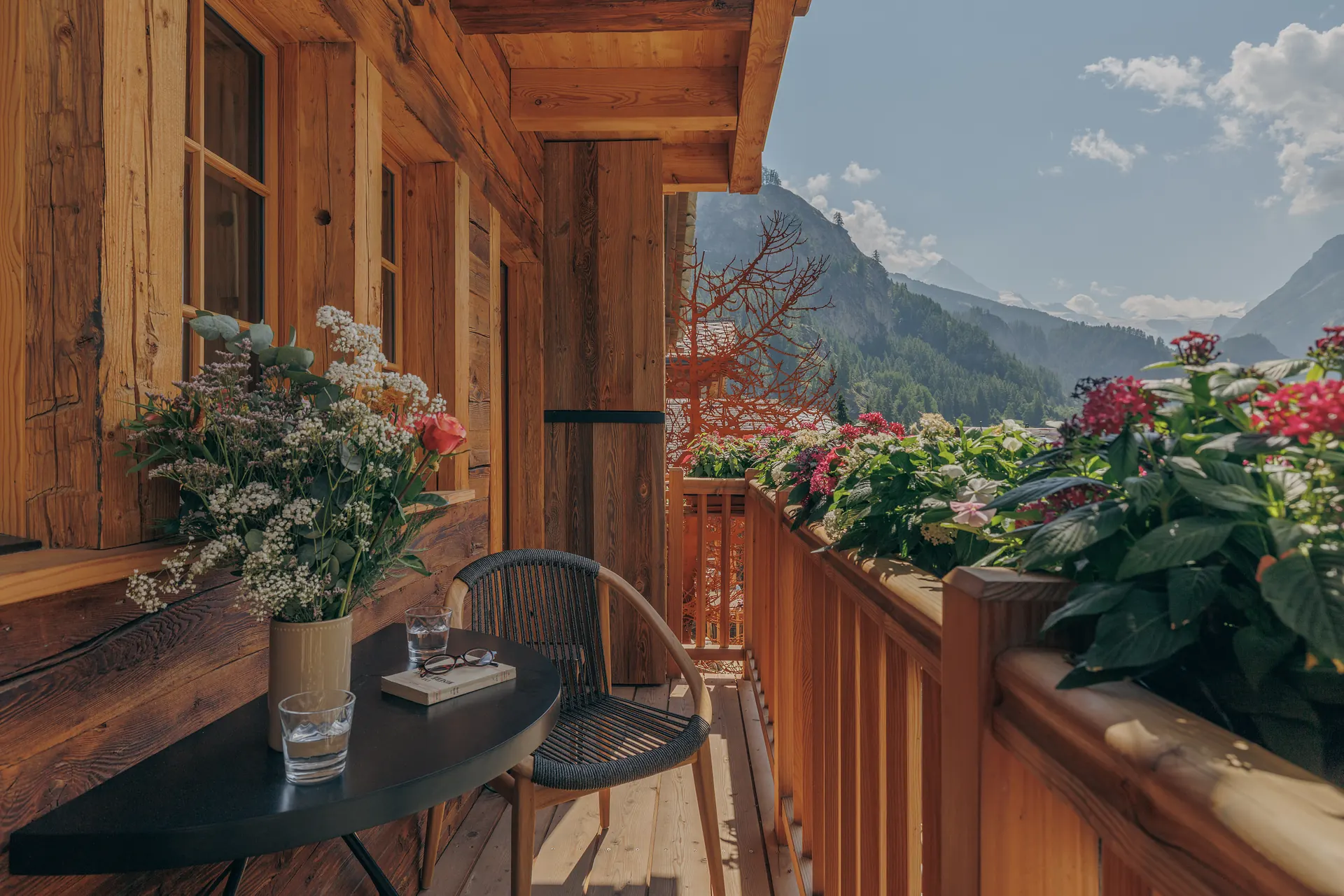 Wooden balcony with a small table, rope chair and flower boxes overlooking an alpine valley