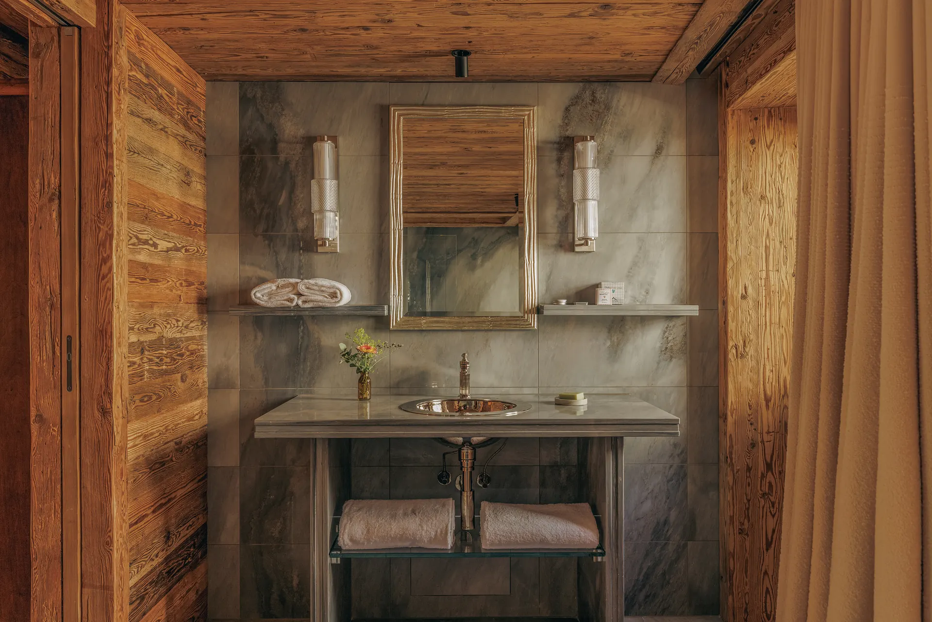 Marble washstand with a brass basin, gold-framed mirror and crystal wall sconces between wood walls