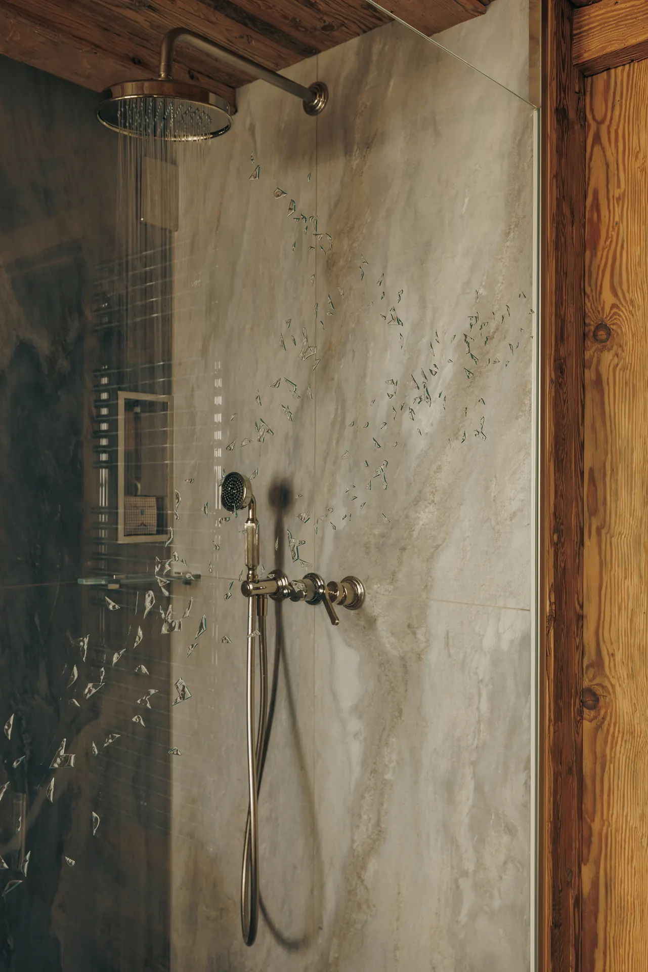 Running rain shower and hand shower on a marble wall, behind a glass panel etched with scattered shards