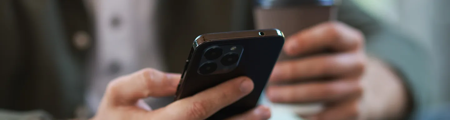 Person holding a smartphone and a cup, focusing on the phone's camera side.