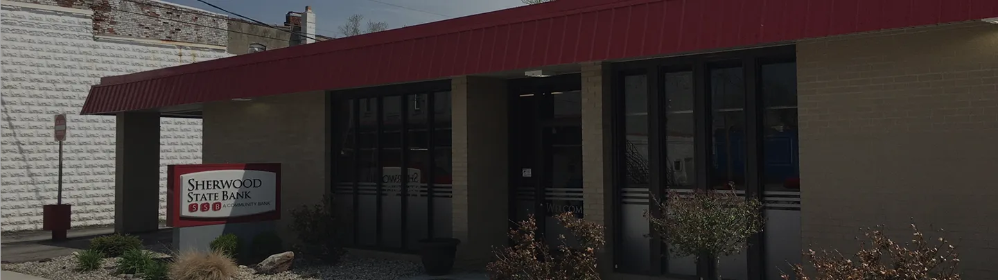 Exterior of Sherwood State Bank building with glass doors and a red roof awning.