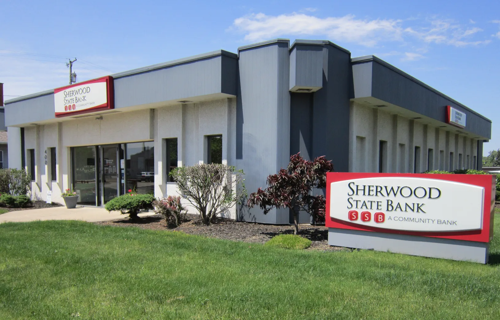 Exterior view of Sherwood State Bank building with large sign on a grassy lawn.