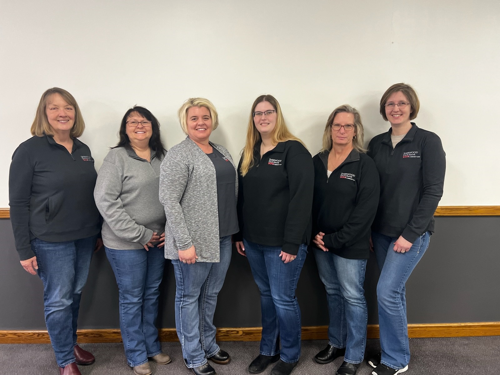 Four women standing in front of a blue wall and red sofa, holding signs with messages like 'Nailed it!', 'Carried the team', 'We cracked the code!', and 'Bigfoots got nothing on me!'