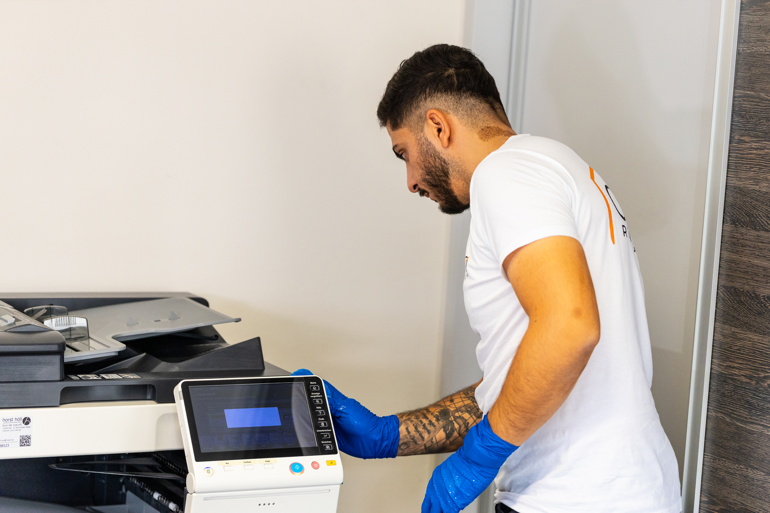 Man wearing blue gloves using the control panel of a photocopier machine.