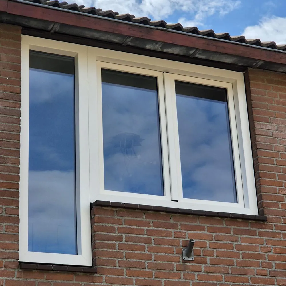 Wit kunststof kozijn met twee vensters in een gevel van rode bakstenen, weerspiegeld de blauwe lucht met wolken.
