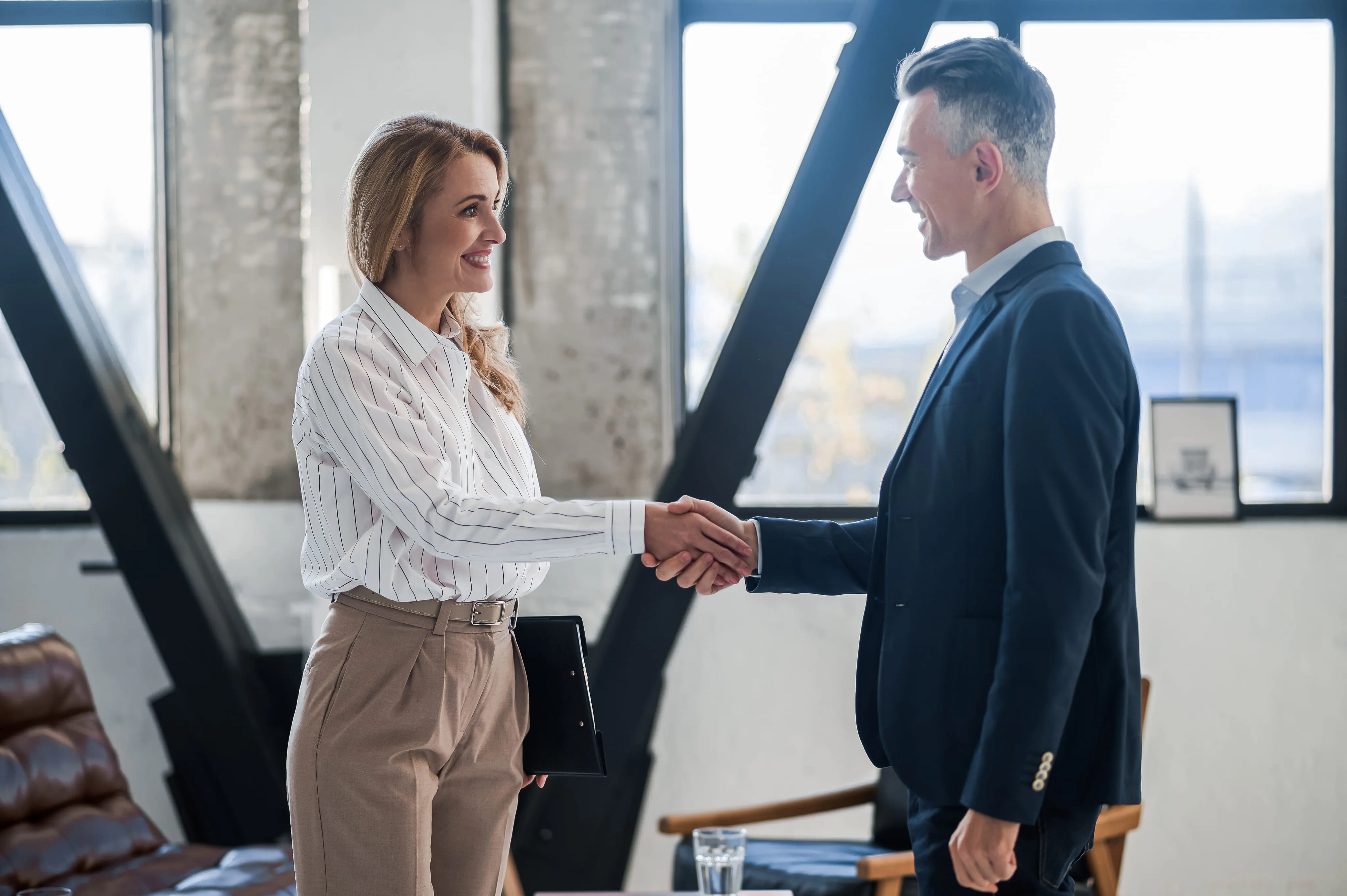 Businesswoman and businessman smiling and shaking hands in a modern office.