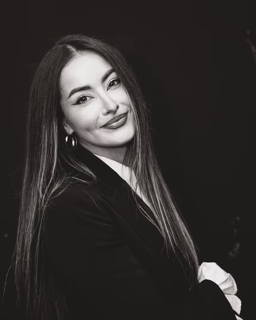 Black and white portrait of a smiling woman with long straight hair wearing hoop earrings and a dark blazer.