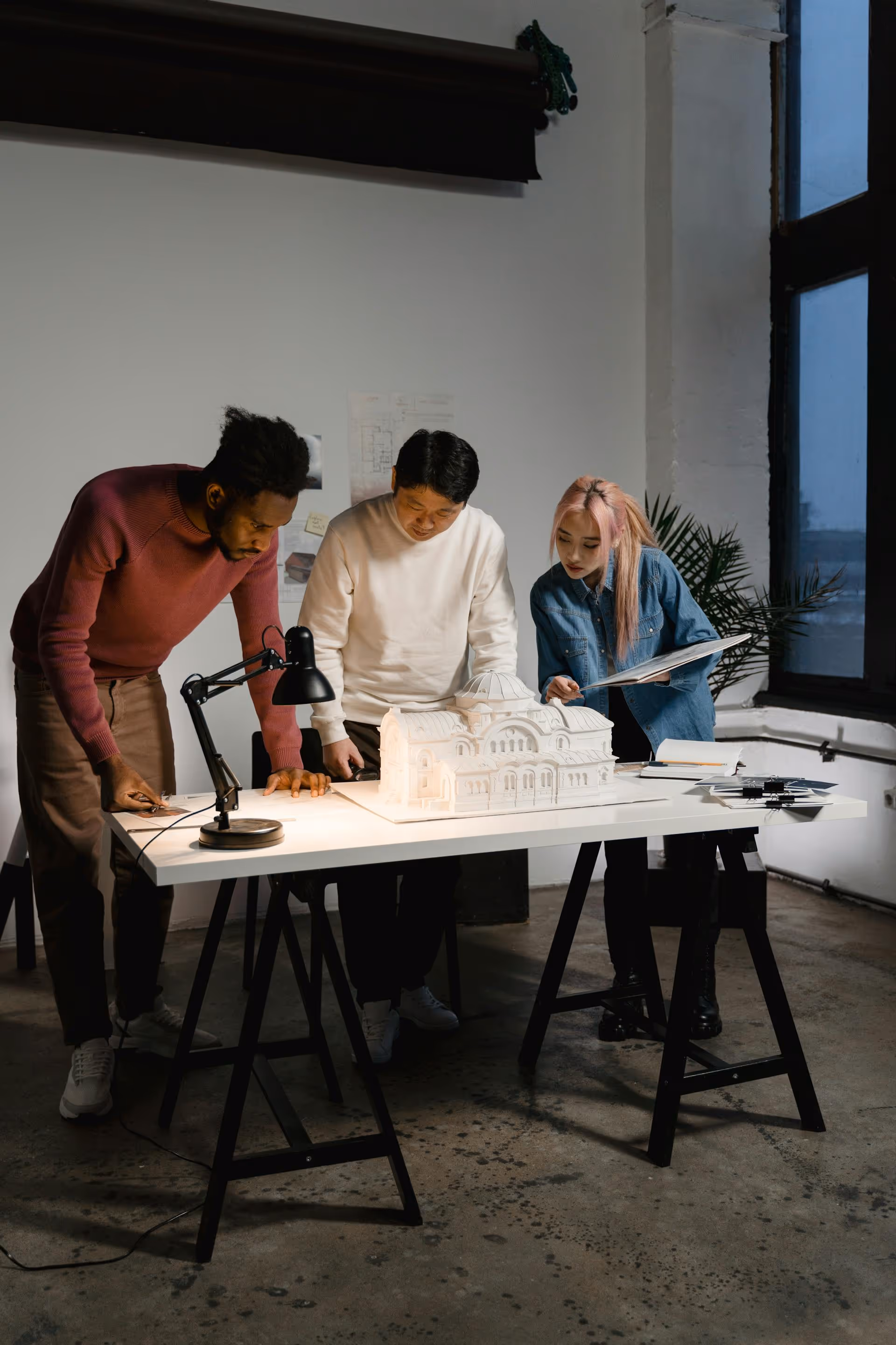 Three architects examining a detailed white architectural model on a table in a studio.