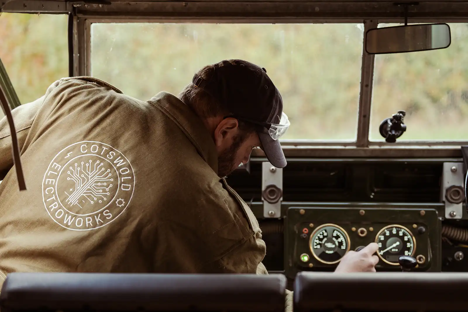 Person in Cotswold Electroworks jacket operating vintage vehicle dashboard