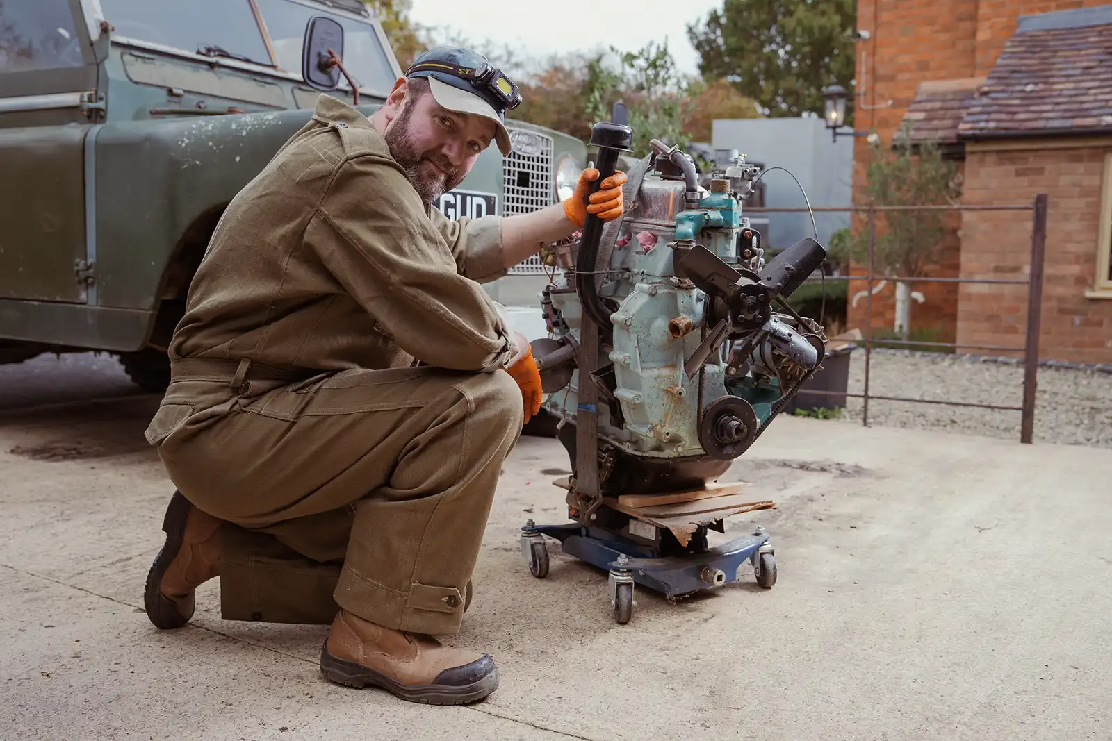 Mechanic wearing work clothes repairs vintage engine next to old military vehicle