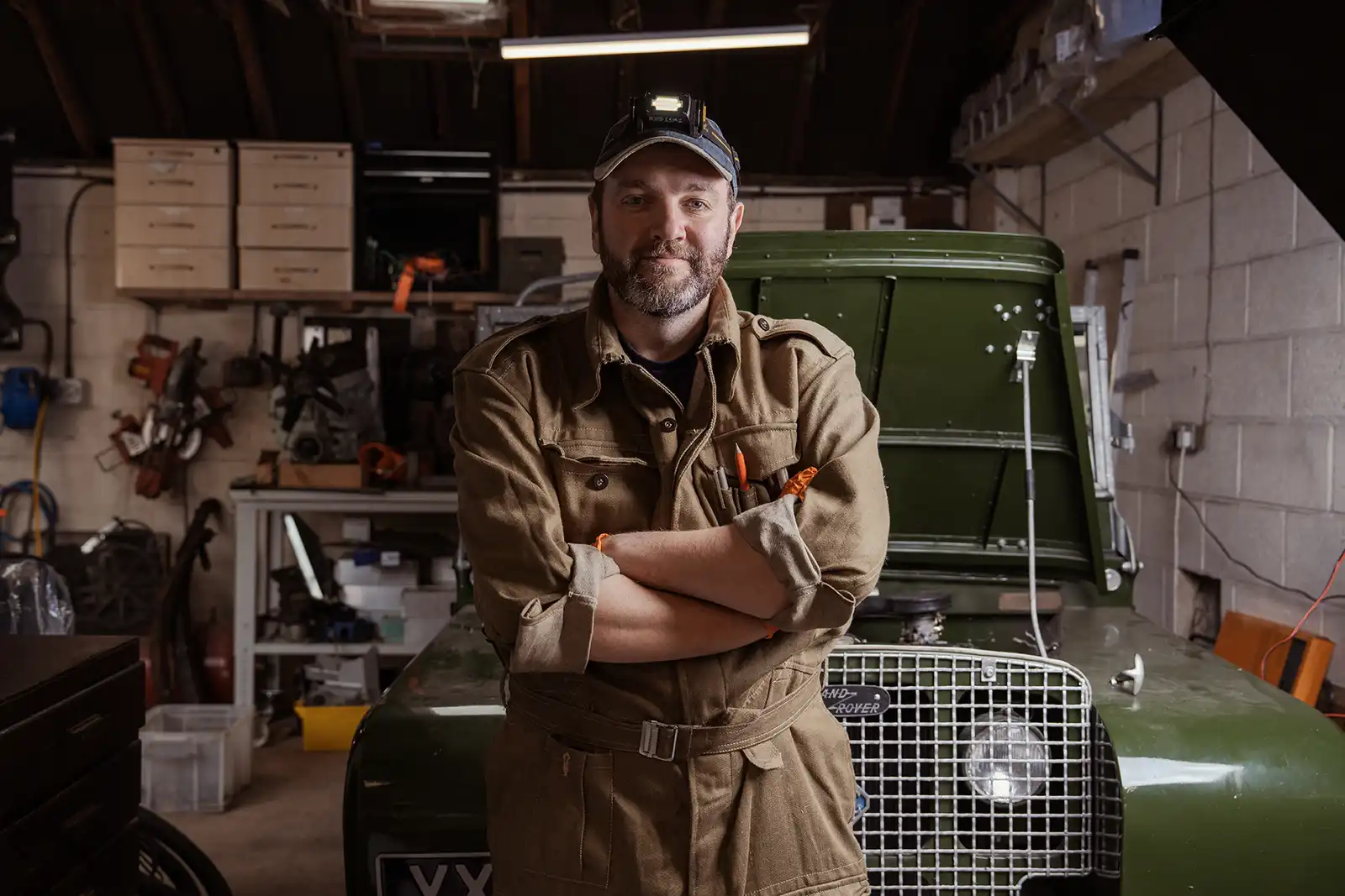 Mechanic in workshop standing near vintage Land Rover with crossed arms