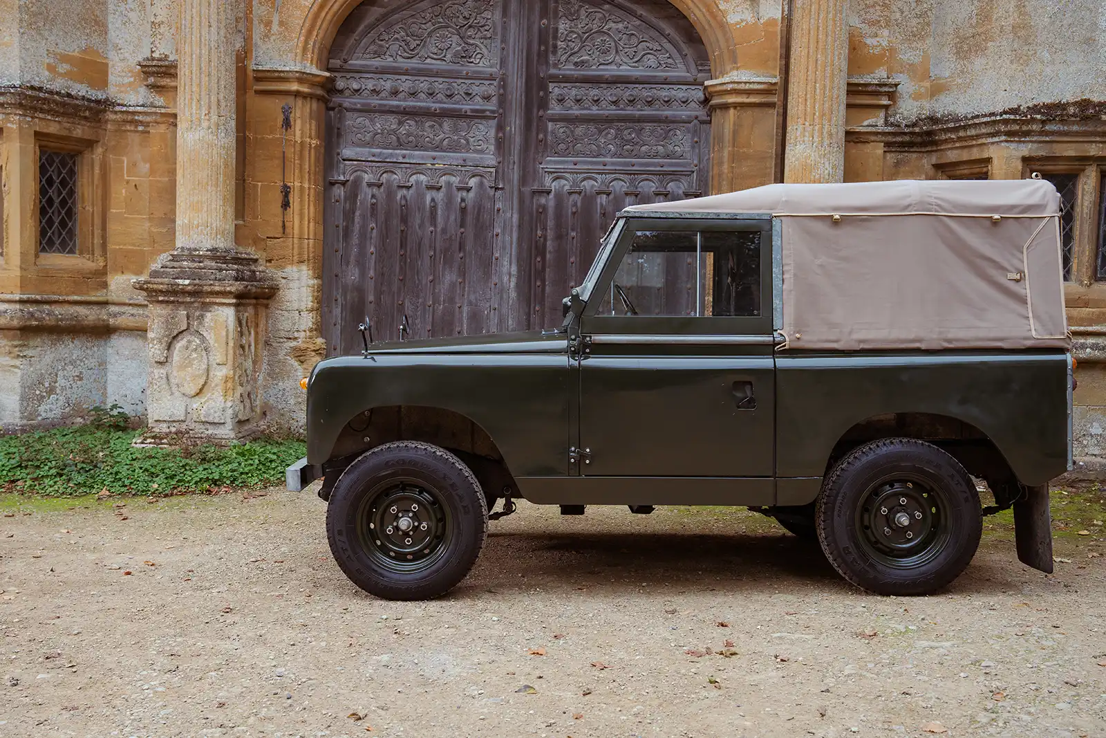 Classic Land Rover with soft top parked in front of ornate stone building