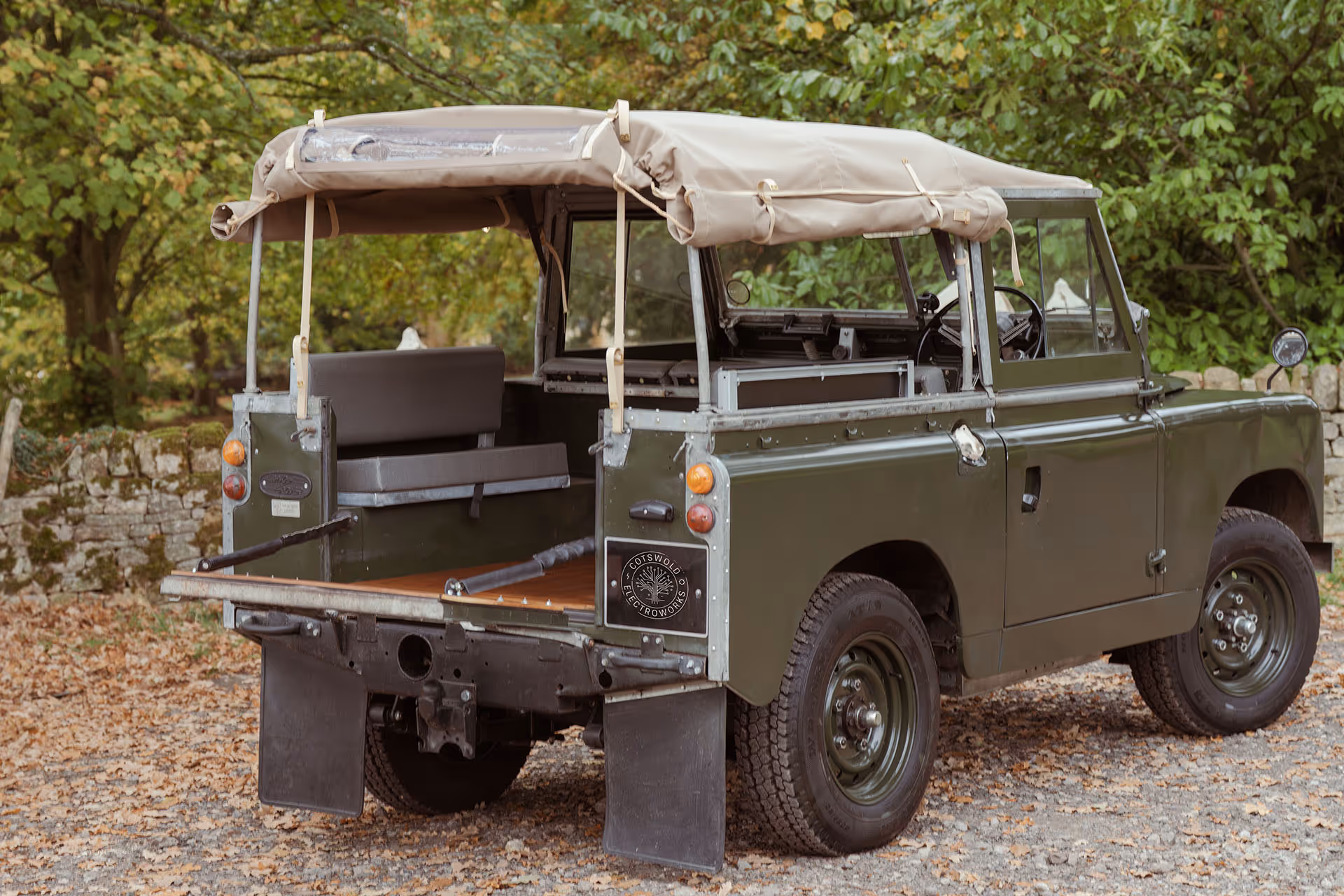 Vintage green Land Rover with canvas top parked in leafy outdoor setting