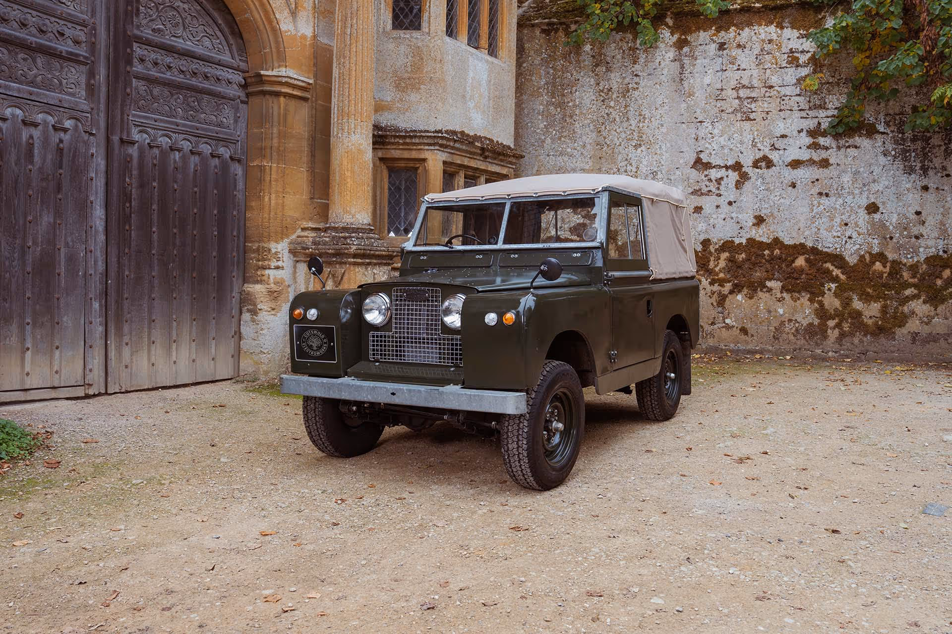 Vintage green Land Rover parked near old stone building with wooden door