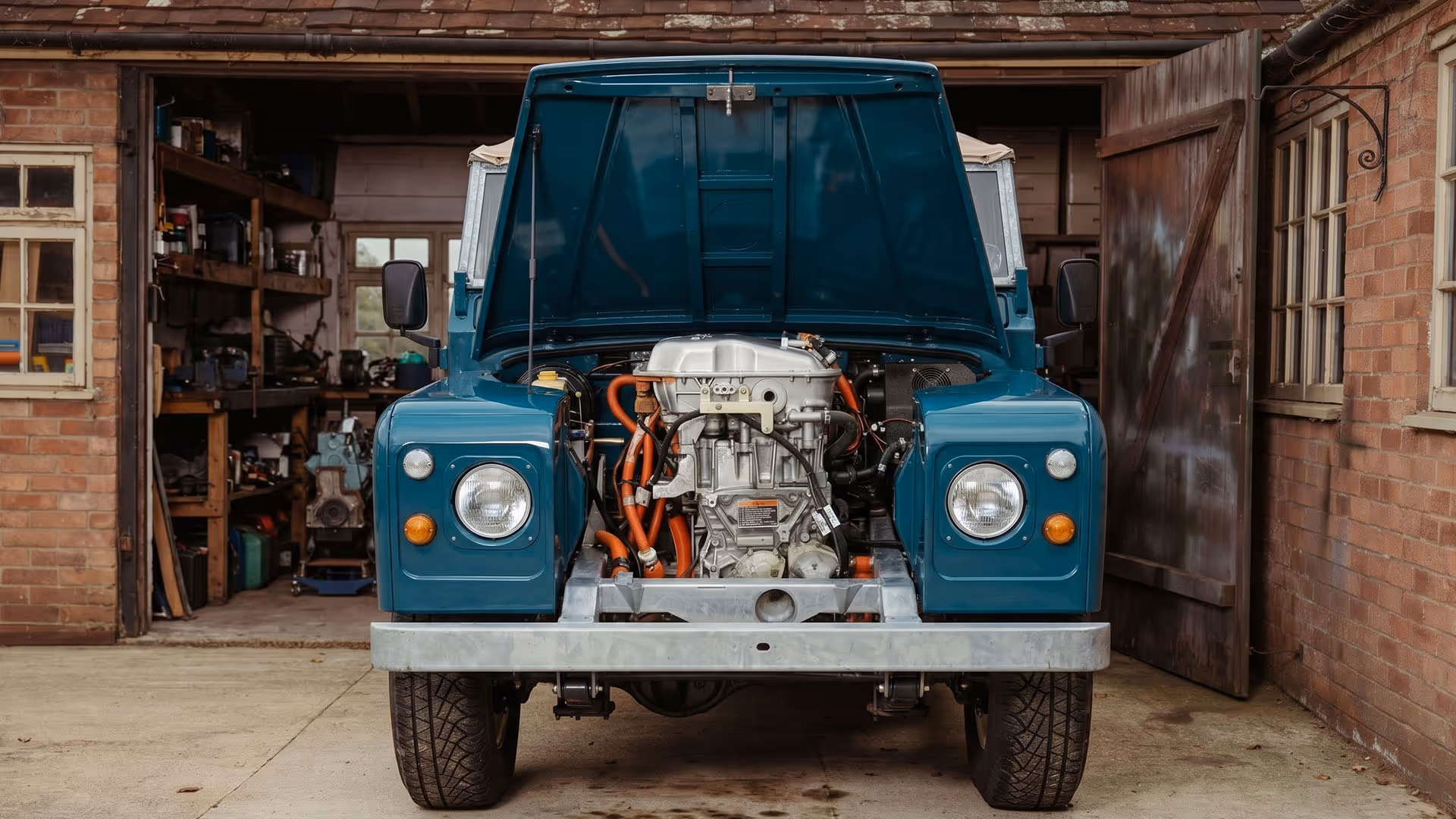 Front view of a blue vintage off-road vehicle with its hood open showing the engine inside a garage.