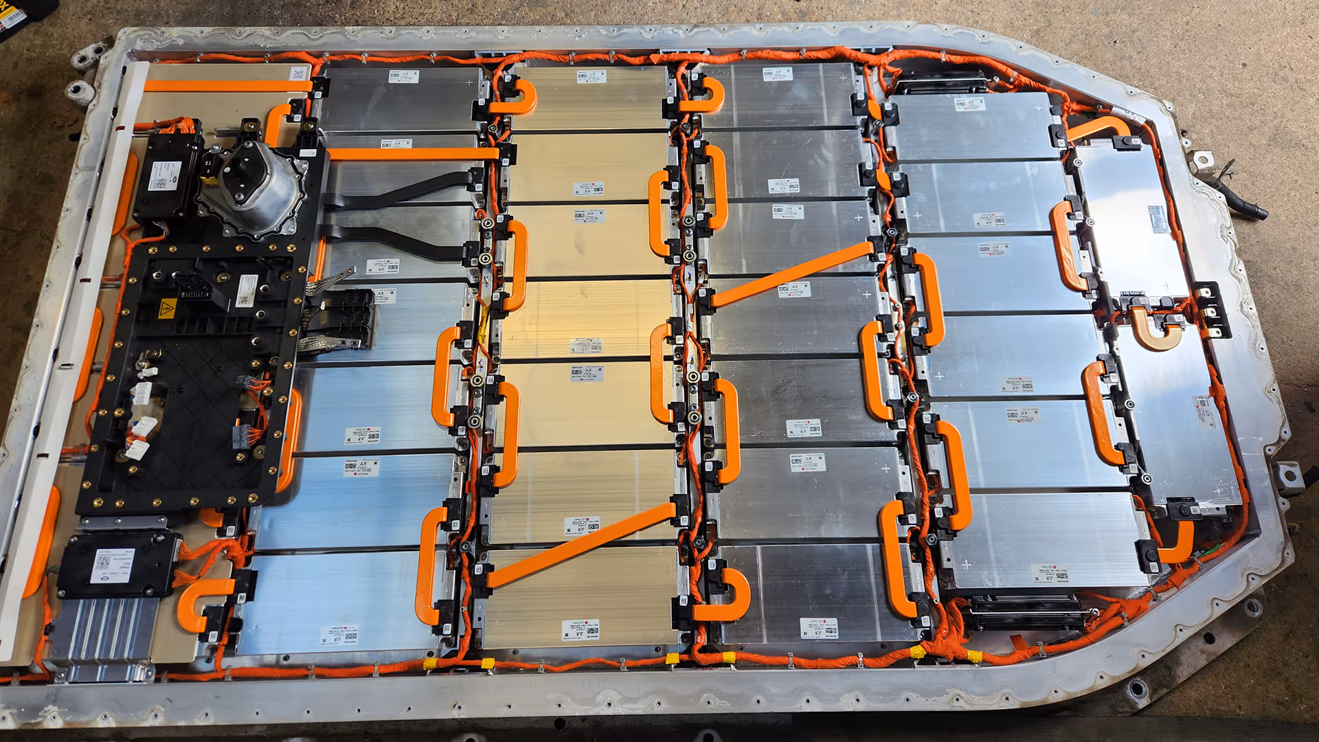 Large electric vehicle battery pack with multiple rectangular cells connected by orange cables.