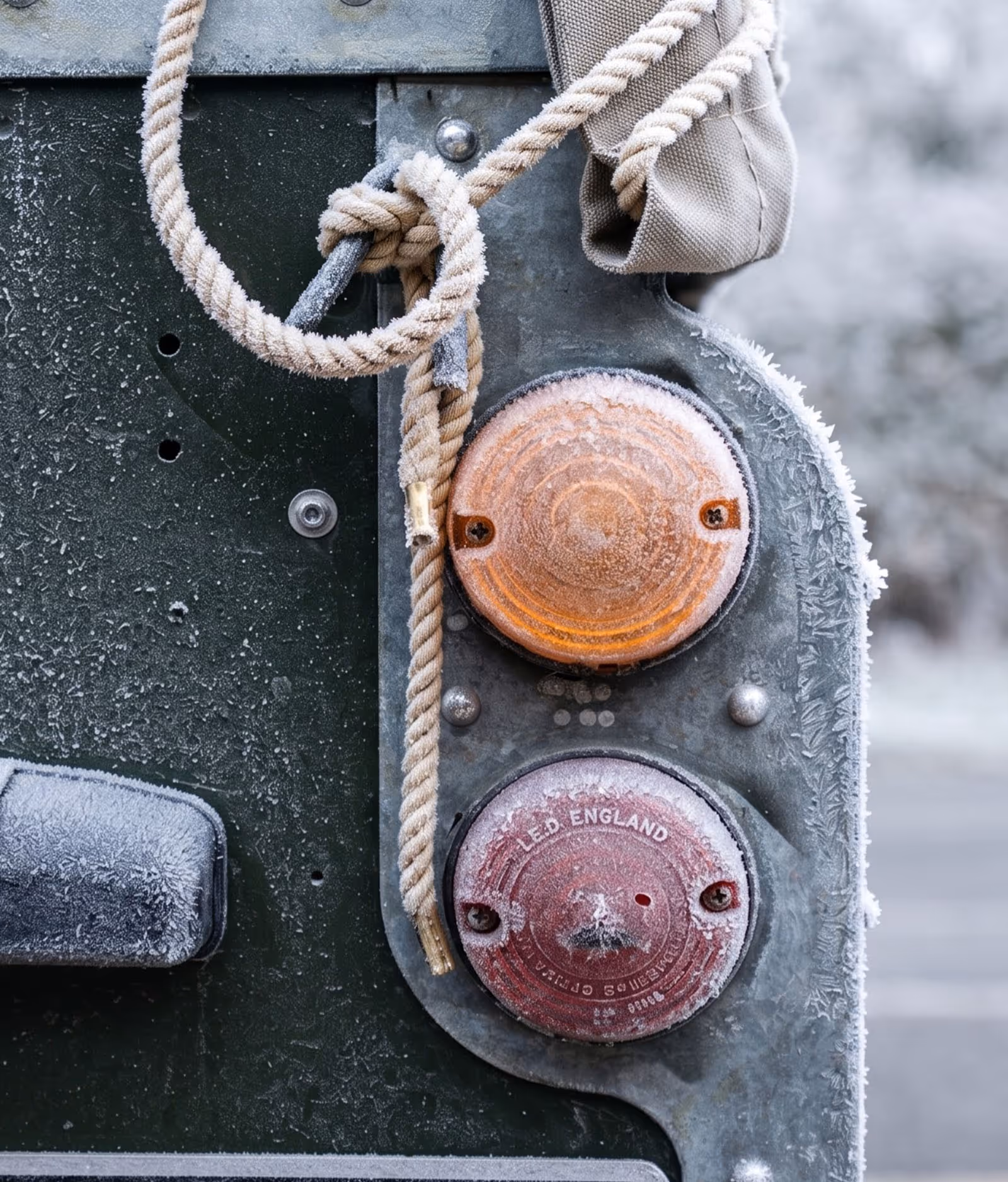 Frost-covered vehicle lights and rope tied to a metal hook on a green surface.