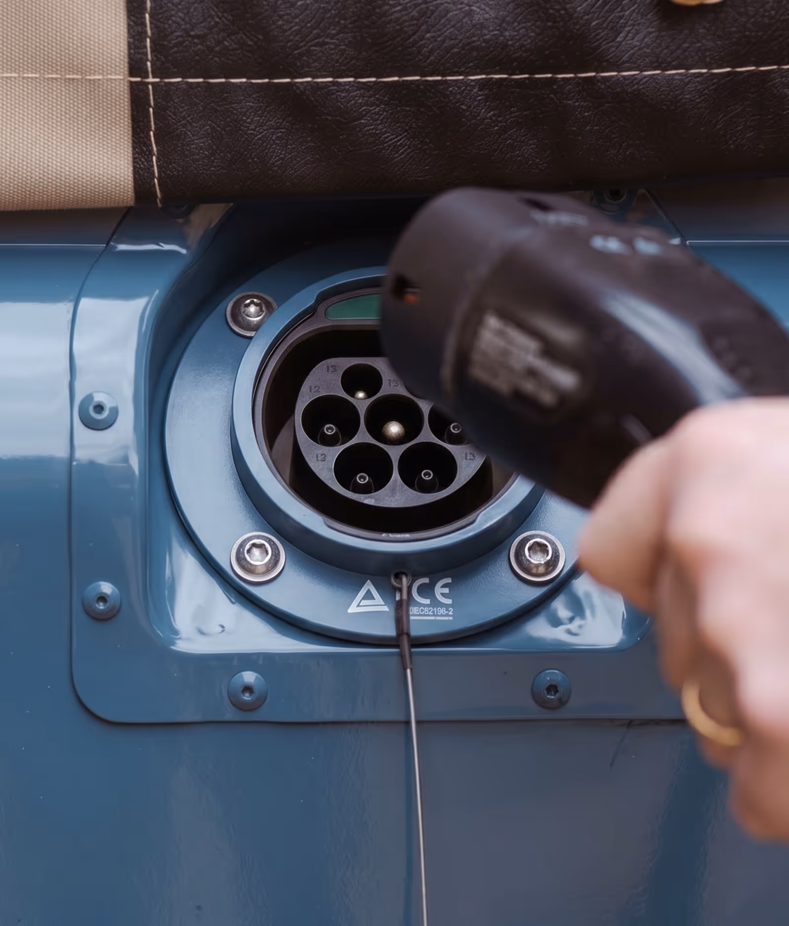 Hand holding a black electric vehicle charger plug near a blue EV charging port.