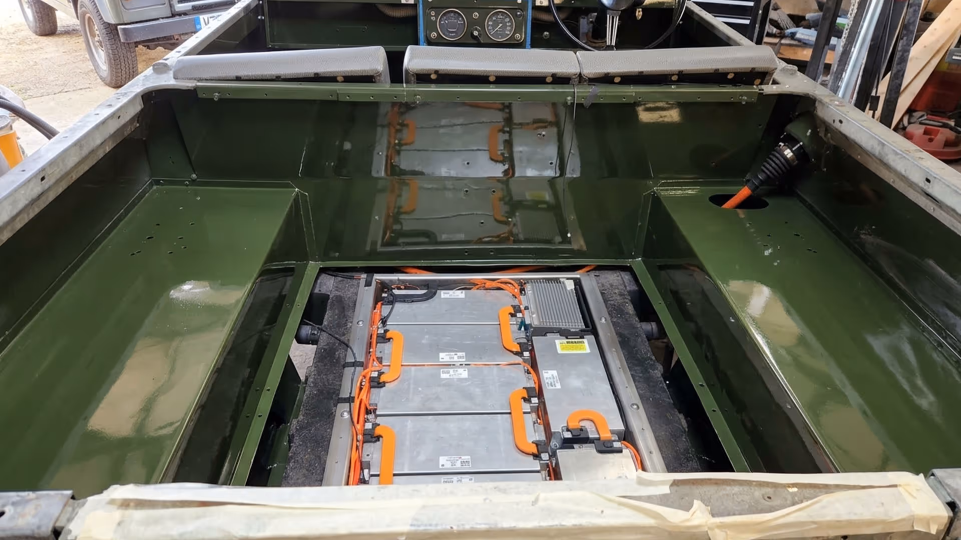 Electric vehicle battery pack installed inside a green metal chassis with orange cables connected.