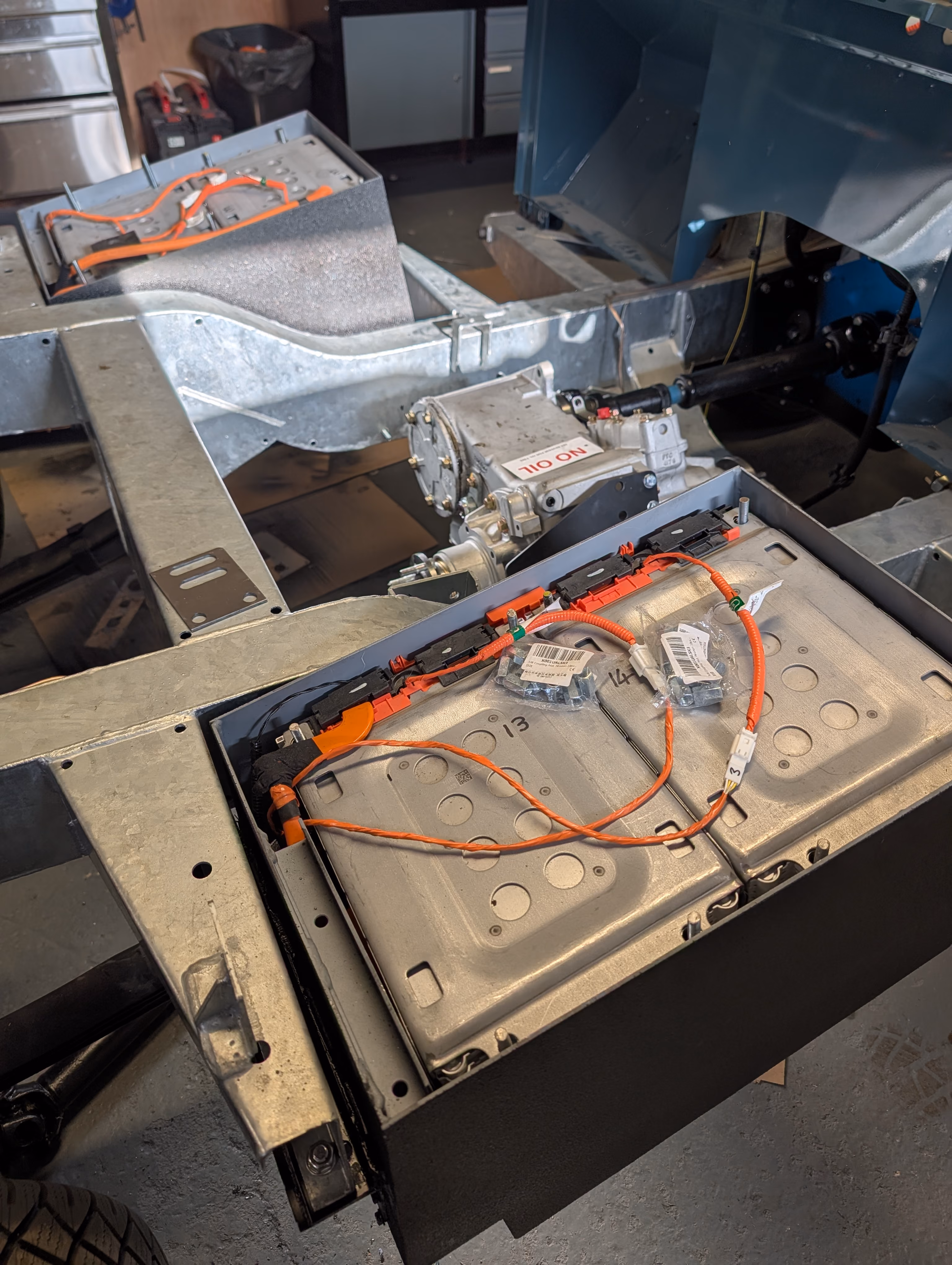Large electric vehicle battery pack with multiple rectangular cells connected by orange cables.