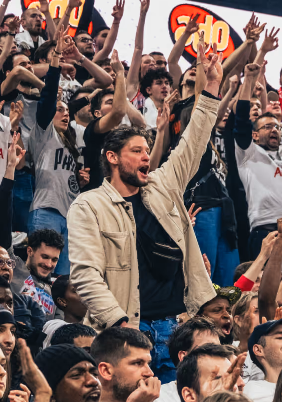 Crowd of enthusiastic sports fans cheering with hands raised in a stadium.