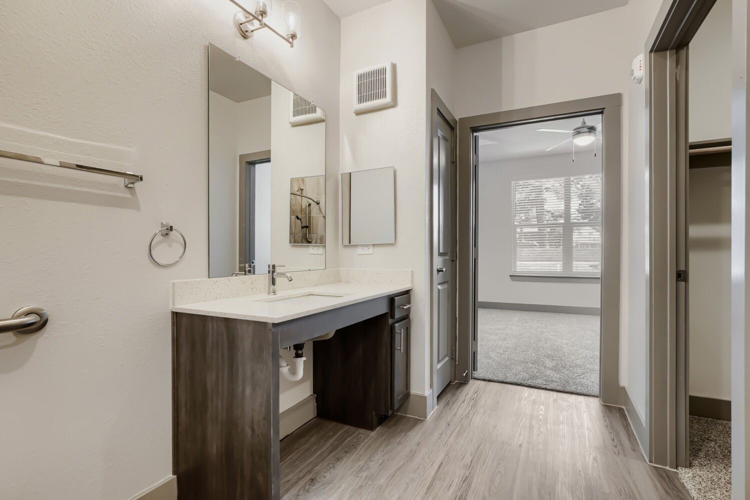 Bathroom with brown vanity with mirror and view into bedroom