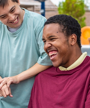 Two young men smiling and enjoying each other's company outdoors, one wearing a teal shirt and the other in a maroon shirt.