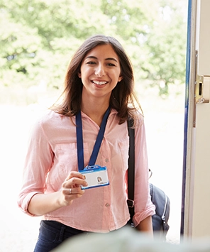 Smiling woman standing at a doorway holding an ID badge with a lanyard.