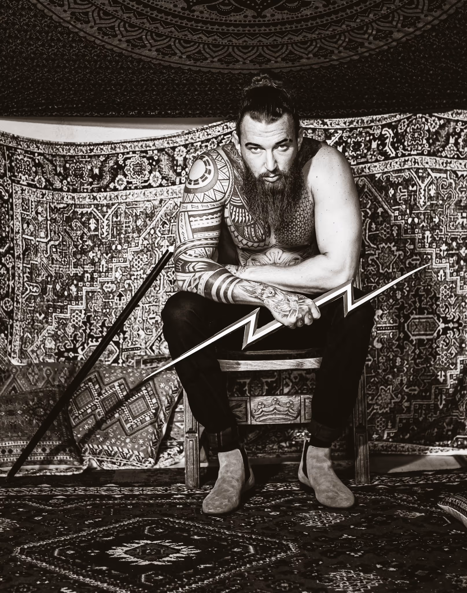 Junge Frau mit lockigem Haar trägt ein graugrünes Hemd und sitzt in einem Garten mit grüner Pflanzenkulisse.