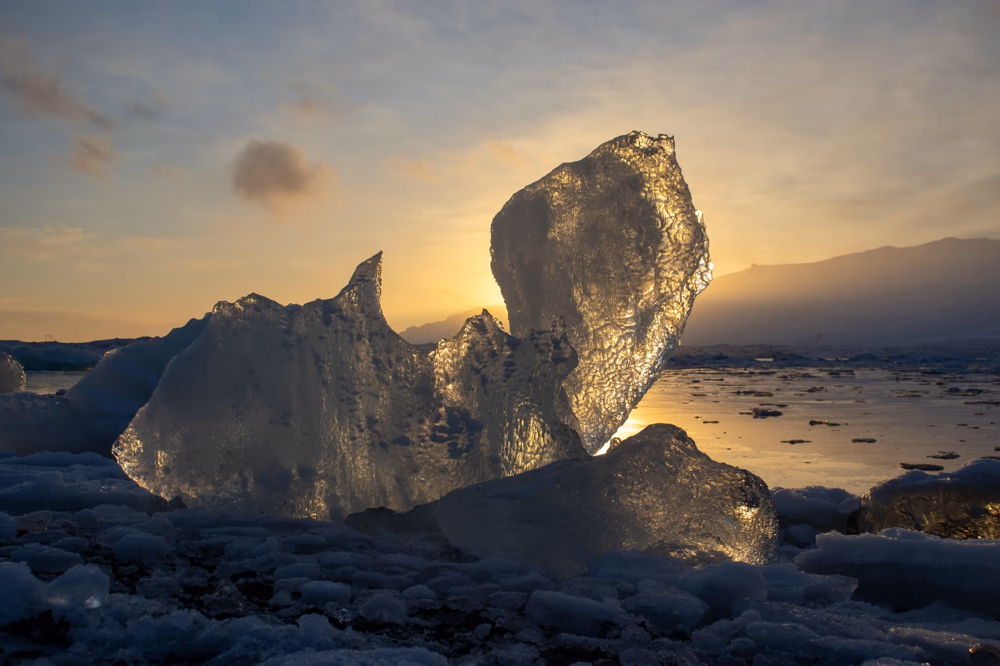 Klares Eis leuchtet im Sonnenuntergang auf einer gefrorenen Landschaft mit Bergen im Hintergrund.