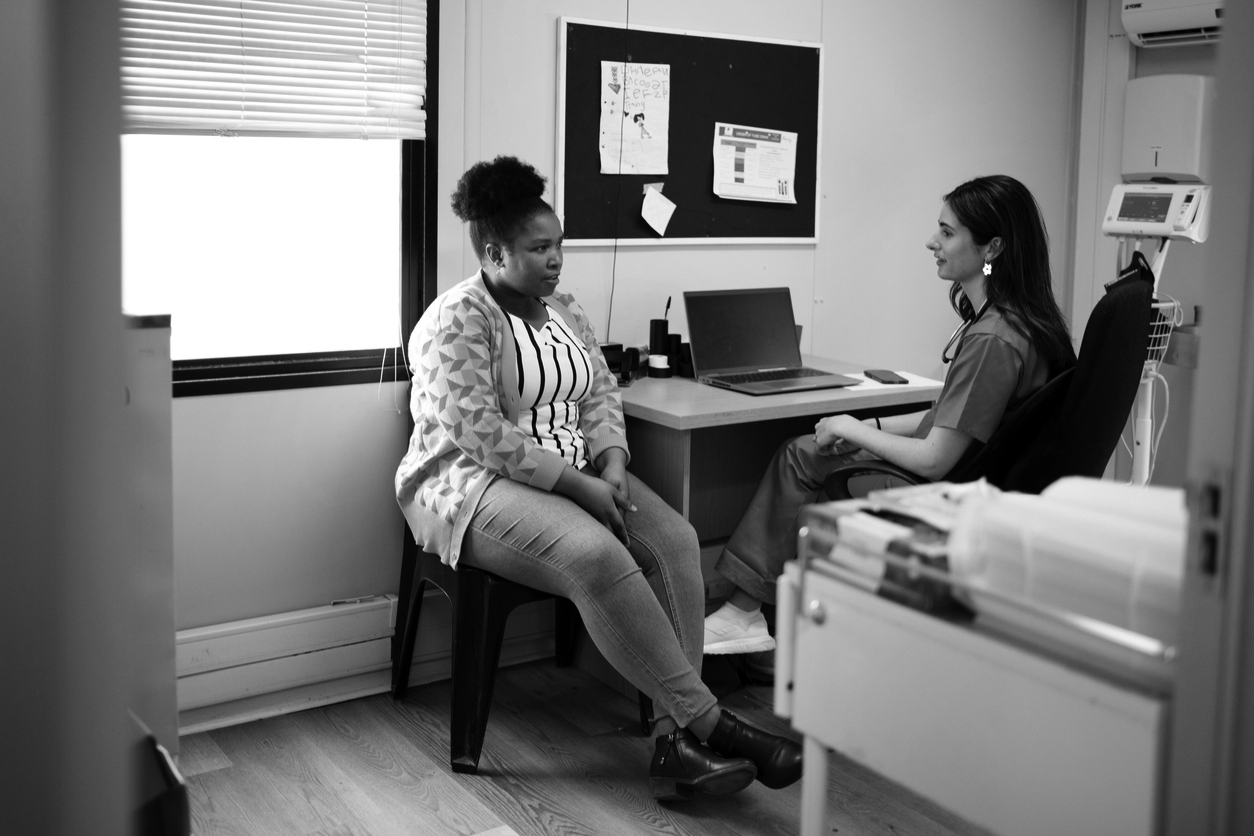 A nurse speaks with a patient in an office room. The two are facing each other and focused on the conversation they are having.