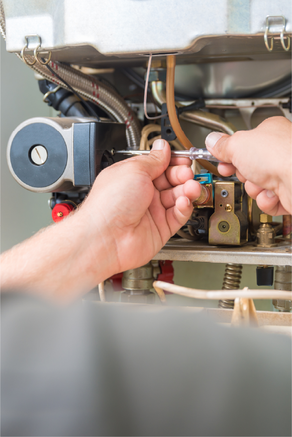 Hands using a screwdriver to repair or adjust components inside a furnace or HVAC unit.
