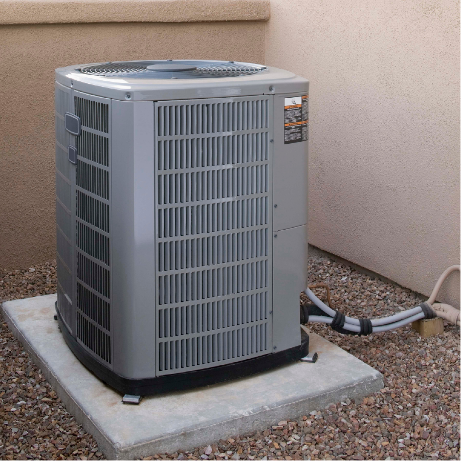 Outdoor air conditioning unit installed on a concrete slab surrounded by gravel next to a beige exterior wall.