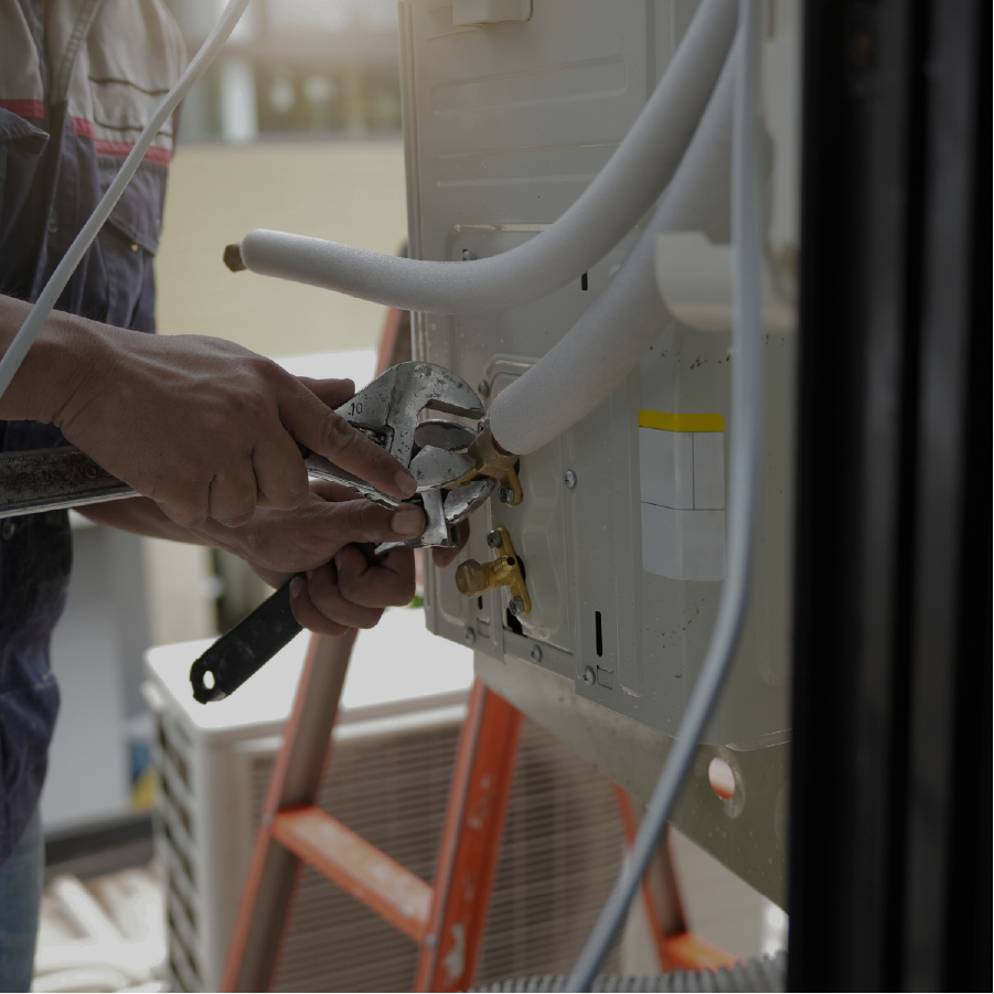 Technician using a wrench to tighten a fitting on an air conditioning unit outdoors.