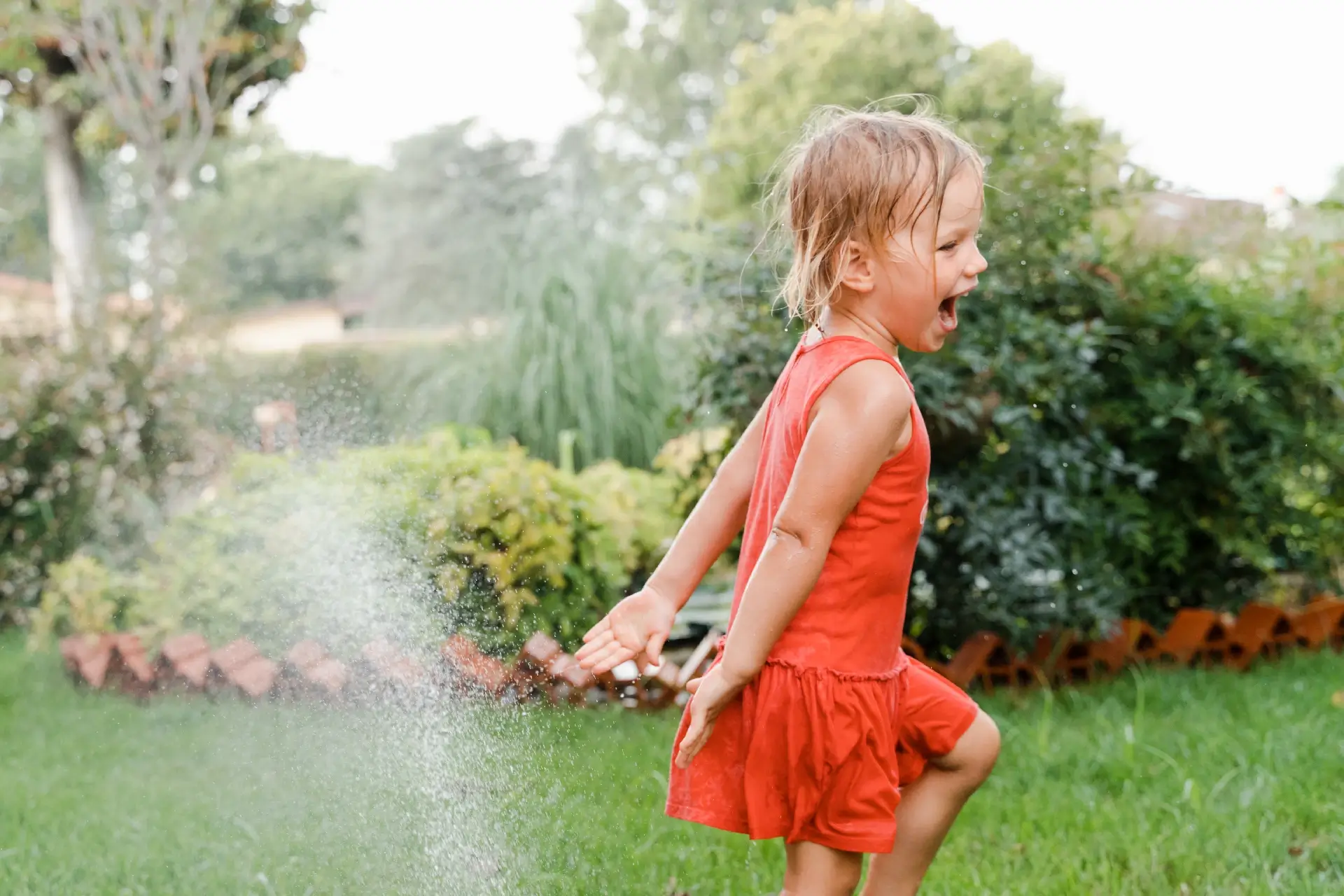 A happy child runs under the splashes of a sprinkler. Time to freshen up.