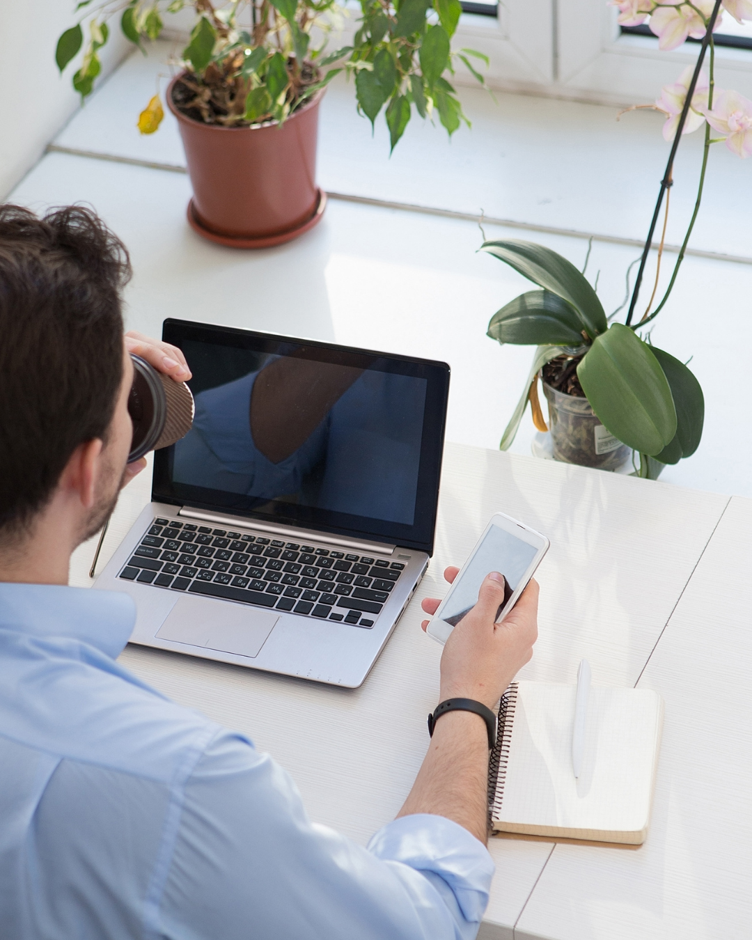 Man aan een werkplek met smartphone en laptop, symbool voor de bereikbaarheid en ondersteuning van Webamigo.