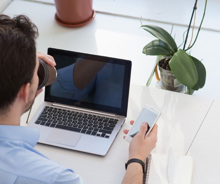 Man aan een werkplek met smartphone en laptop, symbool voor de bereikbaarheid en ondersteuning van Webamigo.