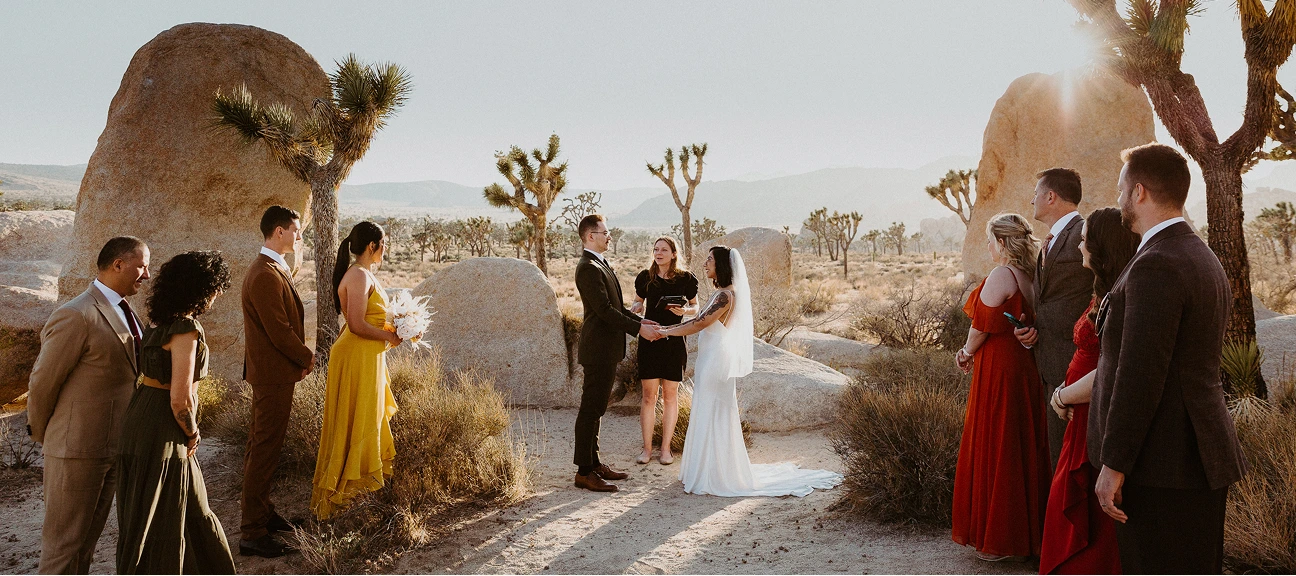 A photo of a wedding ceremony in the desert, bride and groom next to the officiant surrounded by witnessess