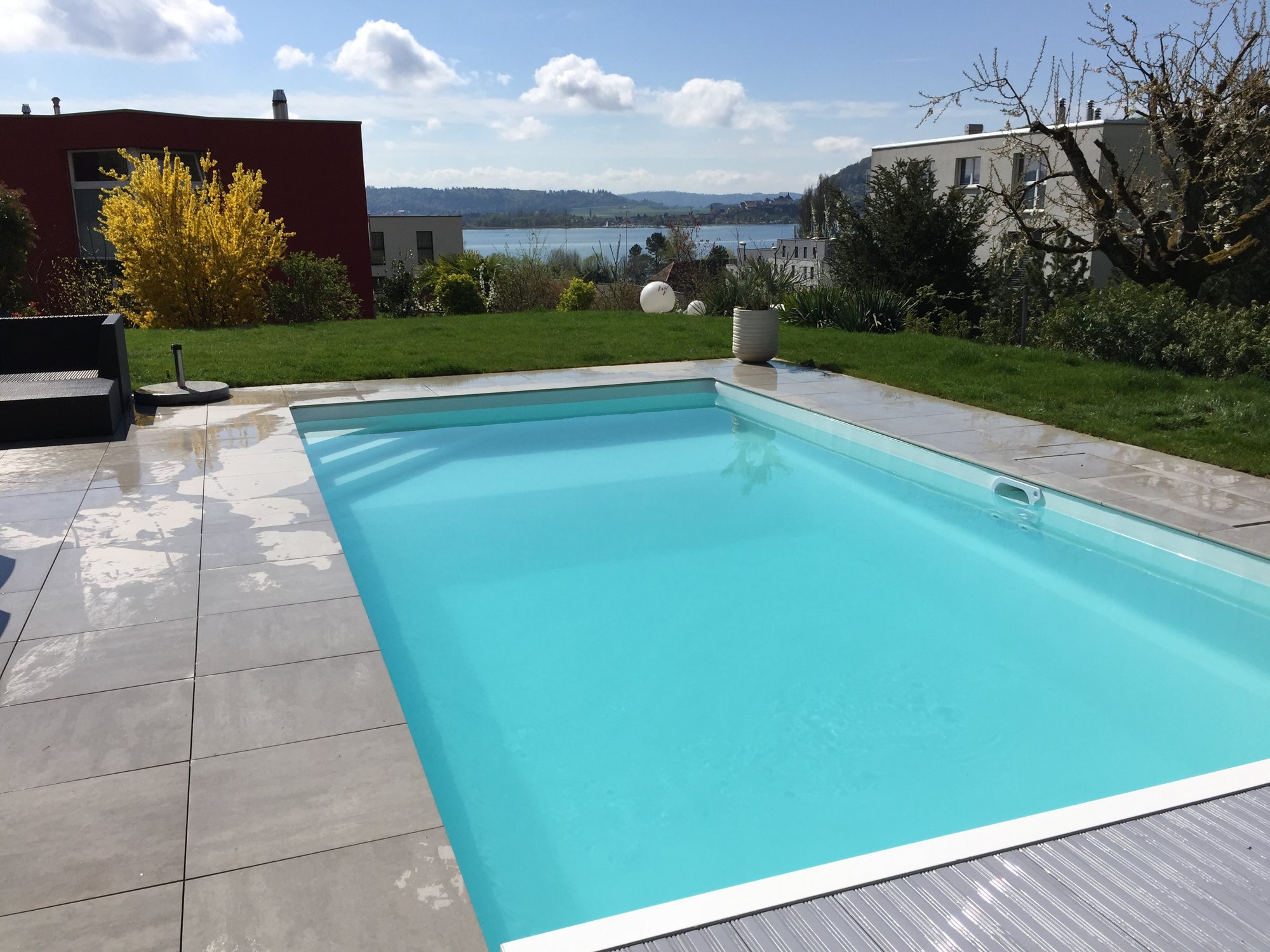 Piscine avec plage en dallage clair et vue sur le lac, réalisée par Espace Piscines et Spas.