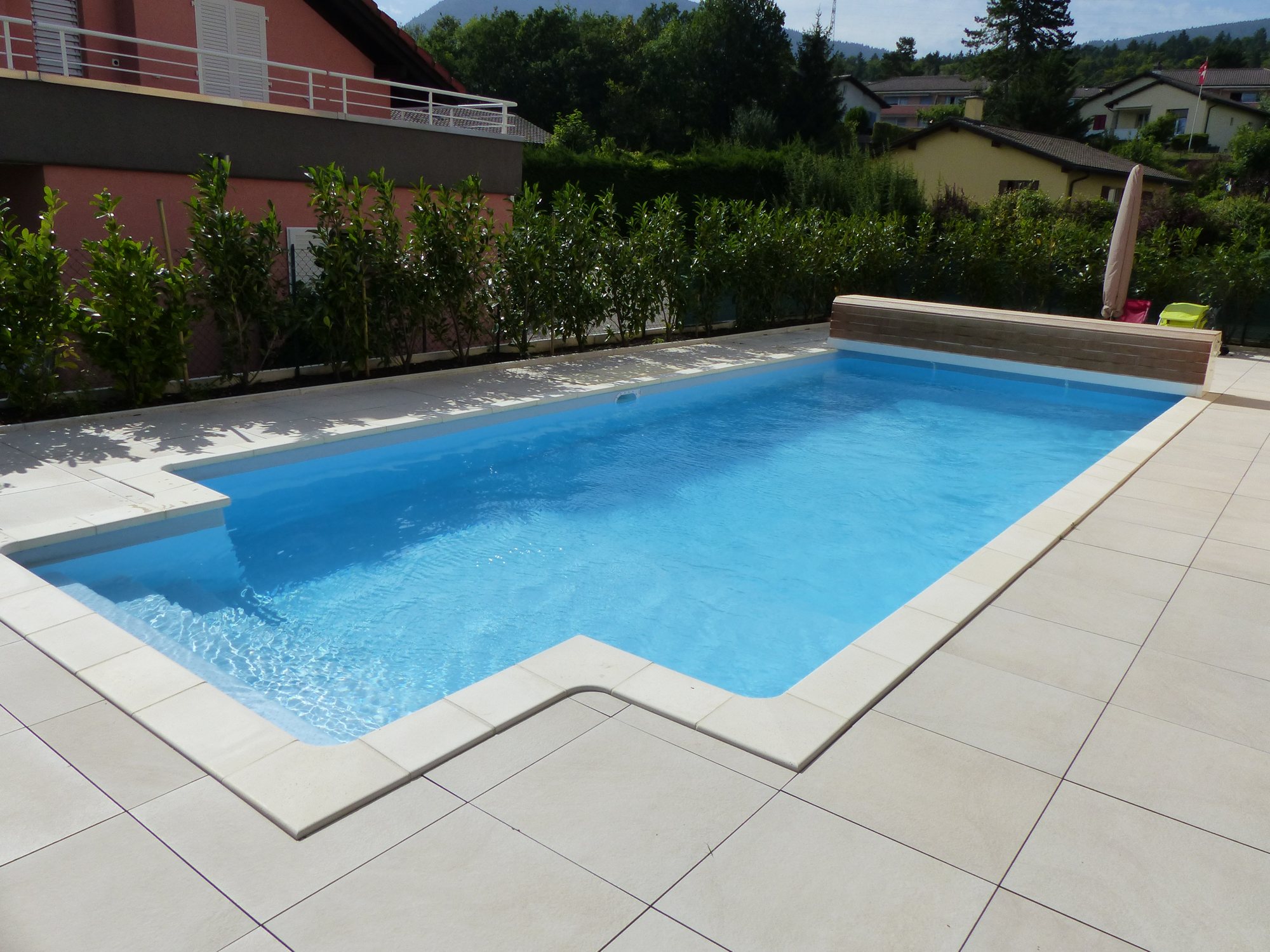 Piscine avec volet immergé et plage en pierre claire, réalisée par Espace Piscines et Spas.