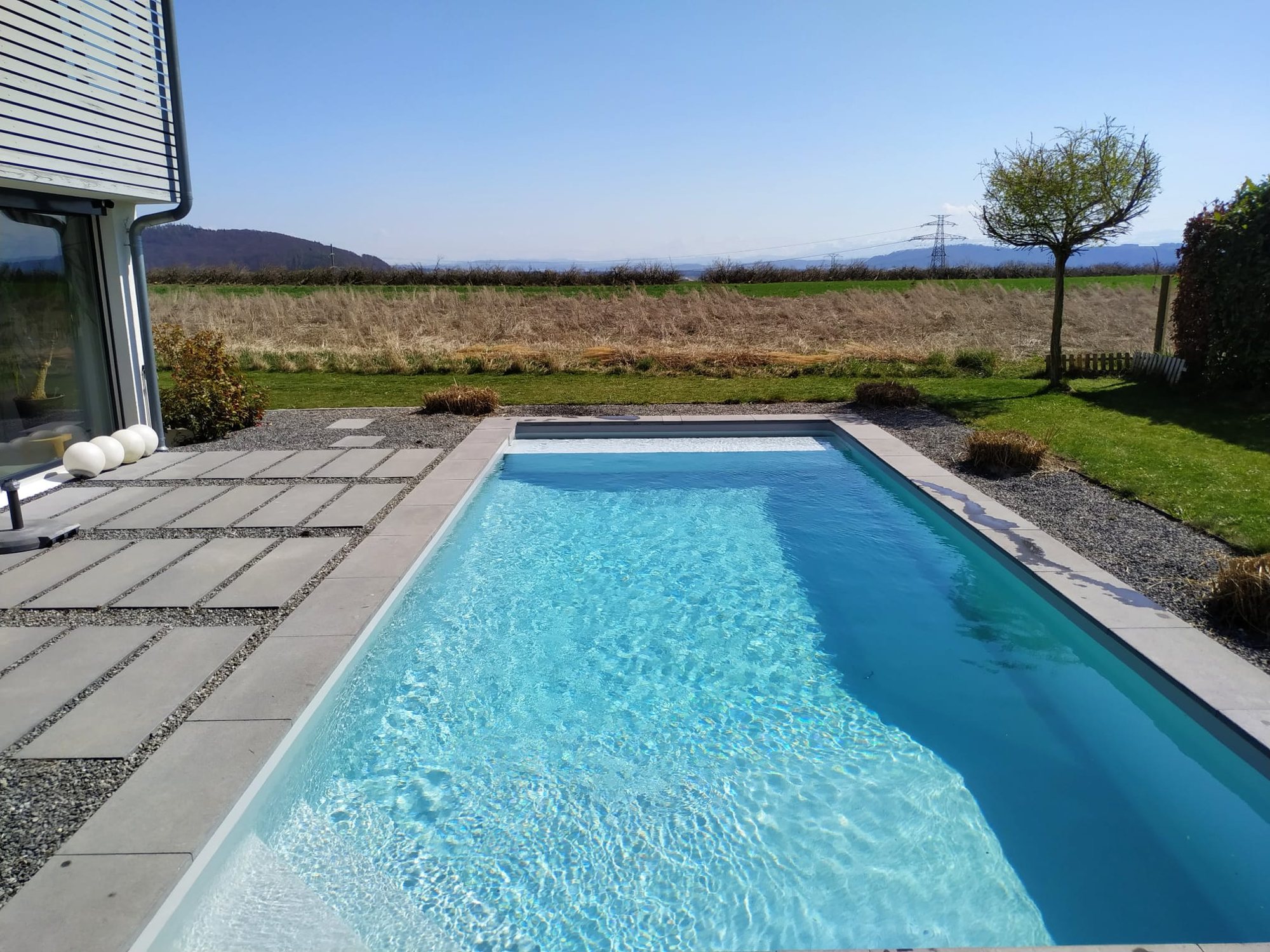 Piscine extérieure avec plage en dalles, réalisée par Espace Piscines et Spas.